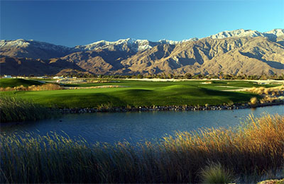 Golf course picture of greens with lake in foreground and mountains in the background