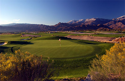 Golf course picture of greens with ahole in foreground and mountains in the background